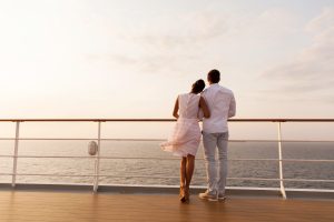 young couple standing on ship deck during sunset