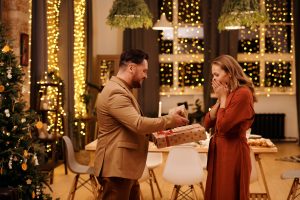a man gives a woman a gift in a holiday settting and she is happy and surprised